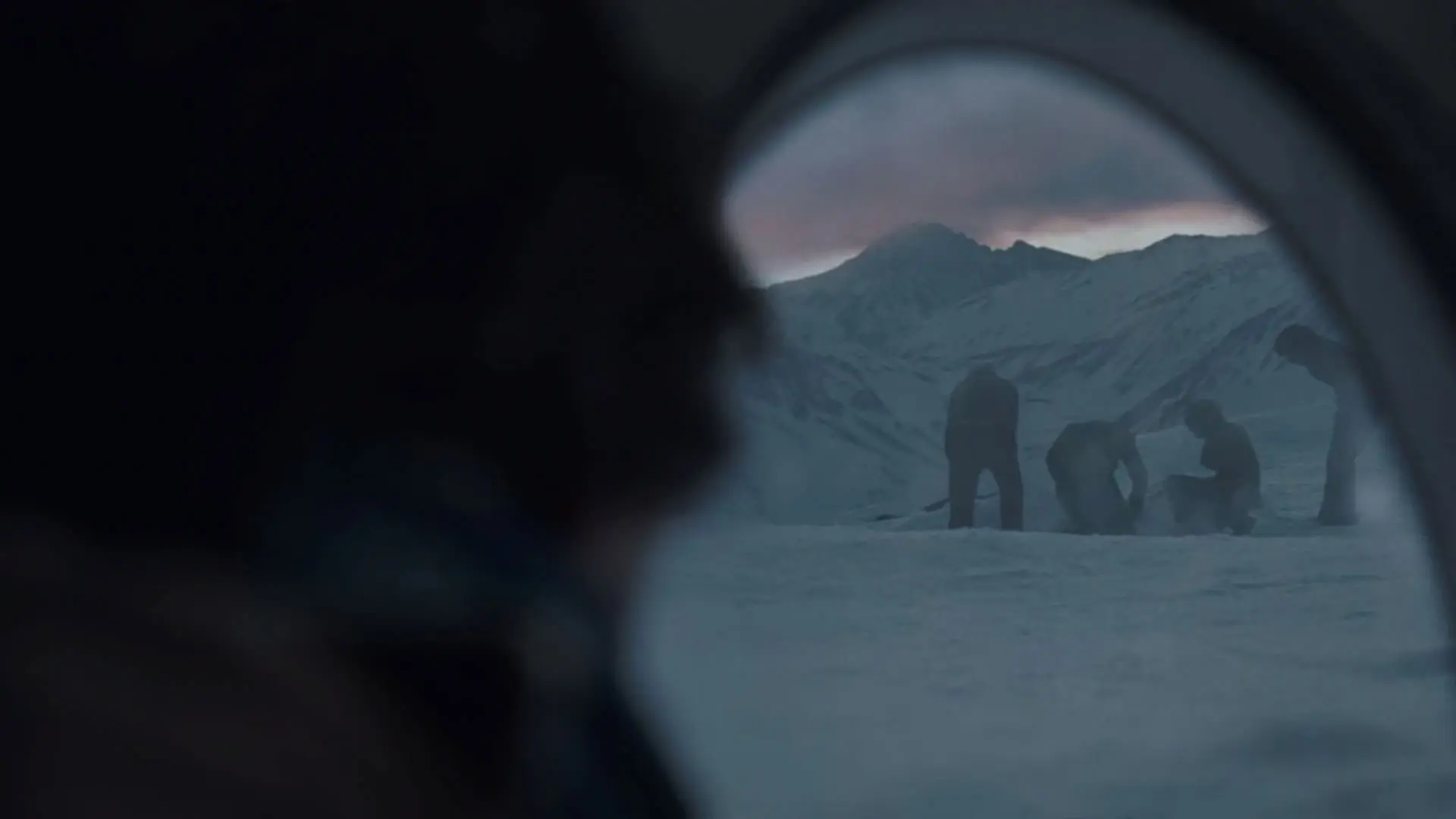مردی از پنجره‌ی هواپیمایی فرود آمده روی زمین به چهار مرد که در دل برف به کاری مشغول هستند نگاه می‌کند در نمایی از فیلم انجمن برف به کارگردانی جی ای بایونا