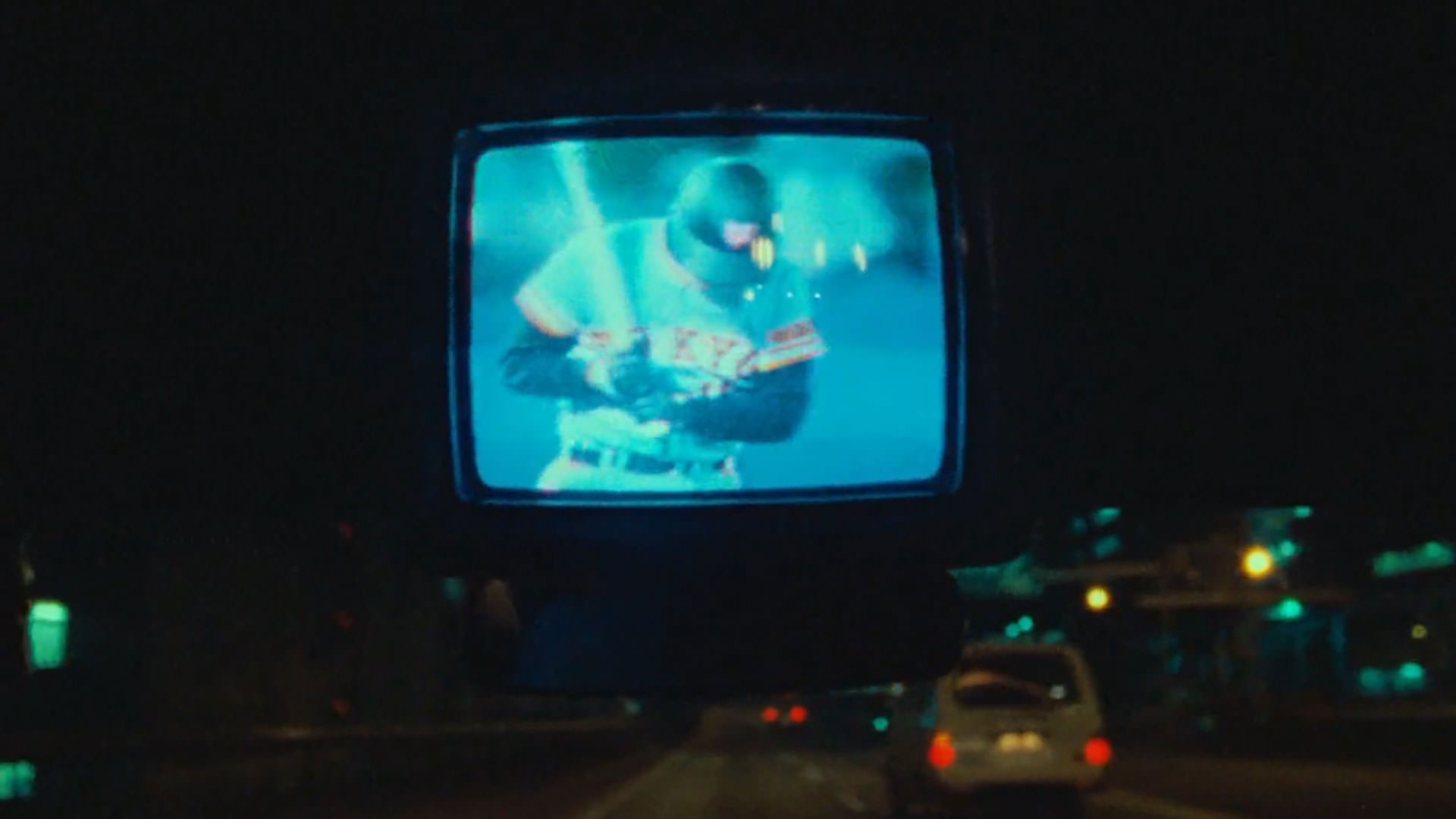 پخش زنده‌ی یک مسابقه‌ی بیسبال داخل یک تلویزیون کوچک داخل یک ماشین در حال حرکت در شب در نمایی از مستند تصاویری از توکیو به کارگردانی ویم وندرس
