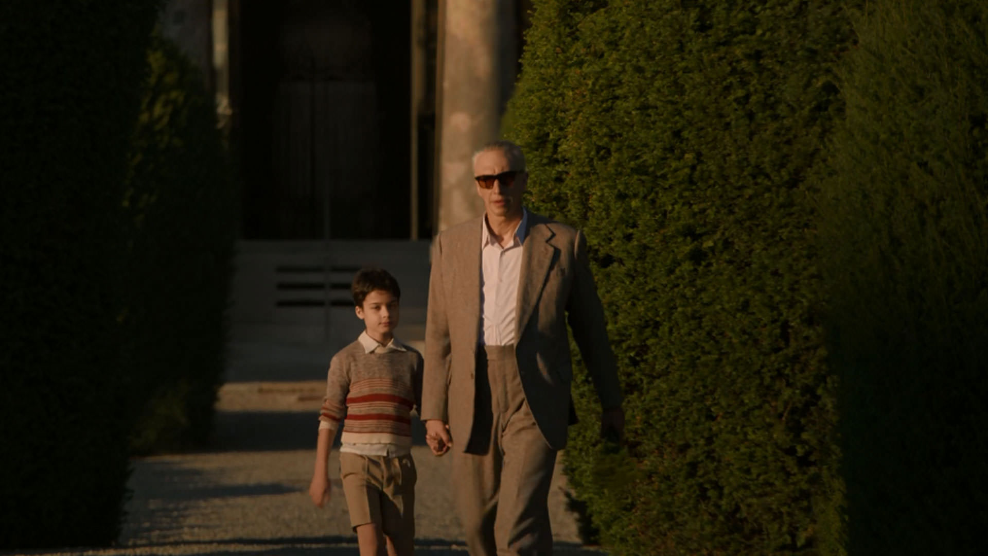 آدام درایور در کنار یک پسربچه از کنار چند درخت می‌گذرد در نمایی از فیلم فراری به کارگردانی مایکل مان