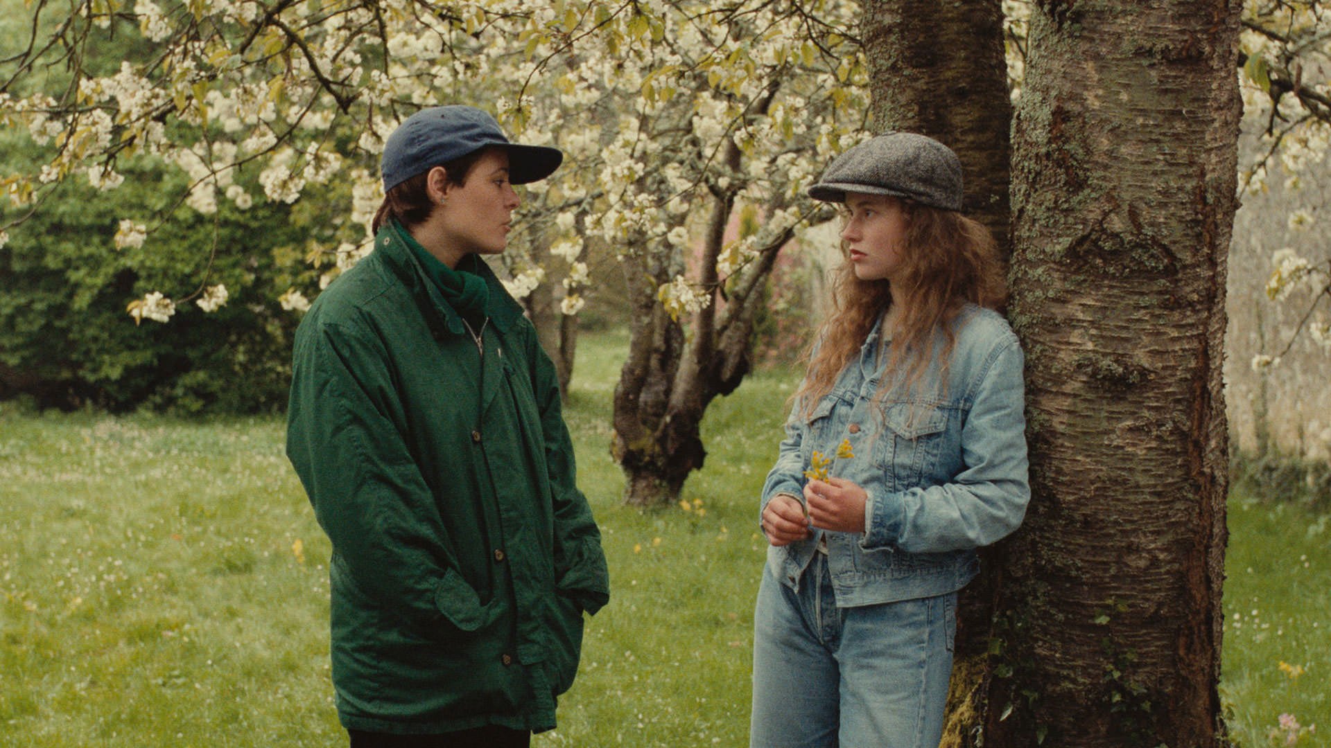 آن تسدرا در صحنه ای از فیلم A Spring Story در مقابل فلورانس دریل با درخت و گل های بهاری پشت سرشان ایستاده است.