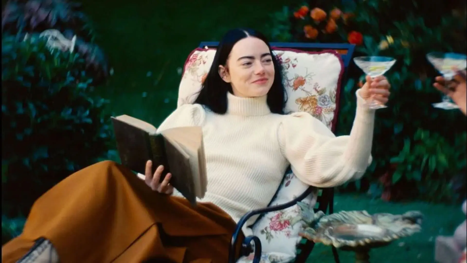 اما استون با یک لیوان نوشیدنی در یک دست و یک کتاب در دستی دیگر با لبخندی بر لب نشسته در آسایش در نمایی از فیلم بیچارگان به کارگردانی یورگوس لانتیموس