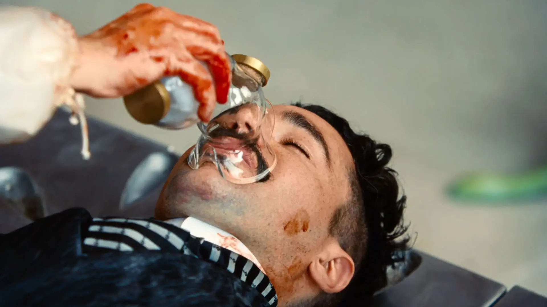 کریستوفر ابوت خوابیده روی تخت جراحی در حالی که دستی خونین ماسک اکسیژن را روی صورت او می‌گذارد در نمایی از فیلم بیچارگان به کارگردانی یورگوس لانتیموس