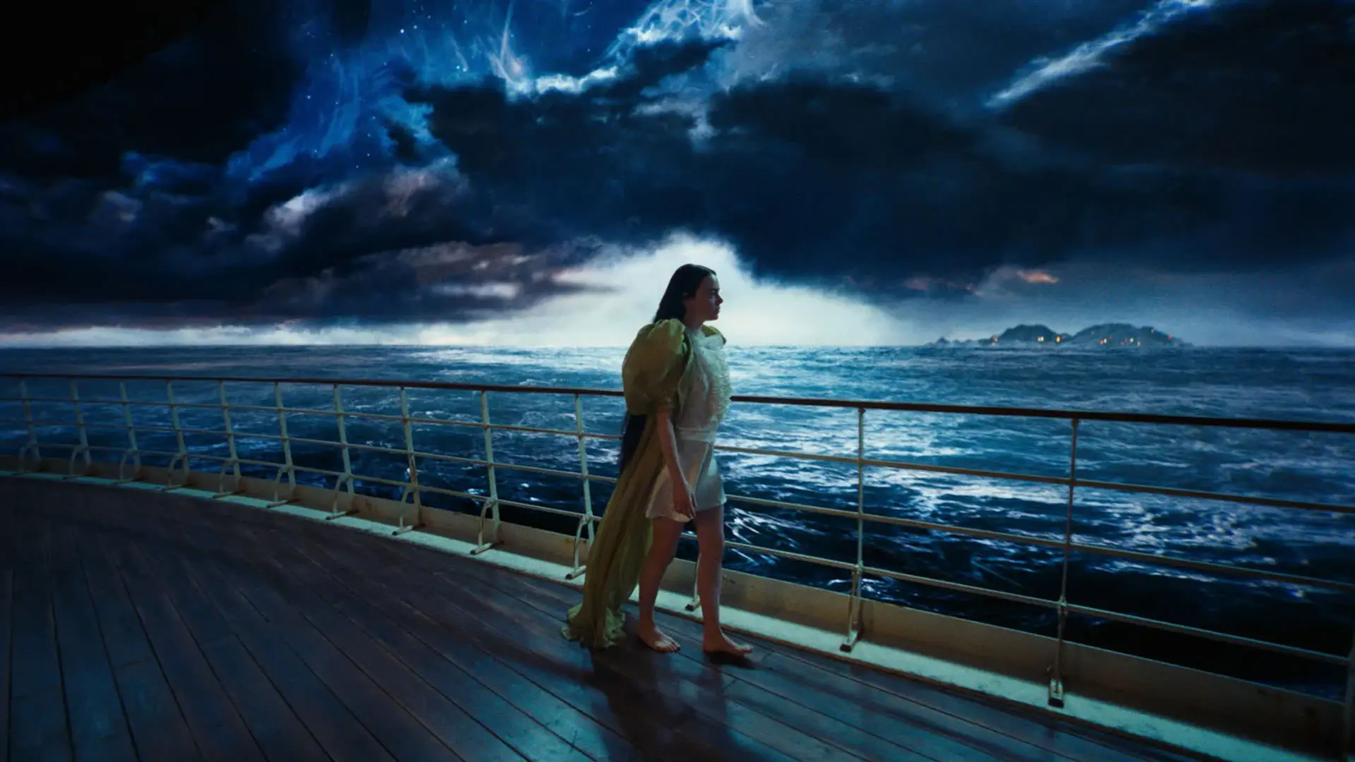 اما استون ایستاده روی عرشه یک کشتی در حالی که آسمان تیره‌ی ابری پشت سرش دیده می‌شود در نمایی از فیلم بیچارگان به کارگردانی یورگوس لانتیموس