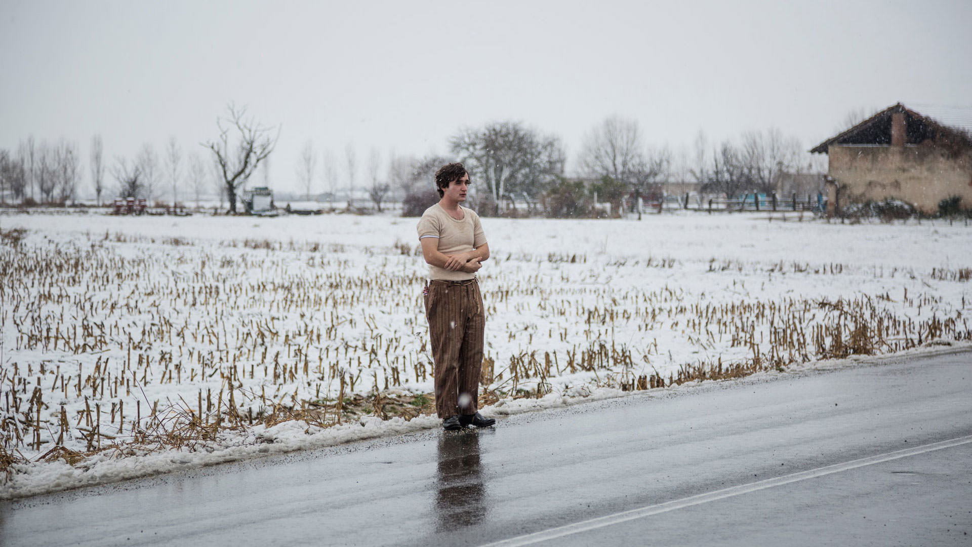 آدریانو تاردیولو ایستاده کنار یک جاده در حالی که بر زمین پشت سرش برف نشسته است در نمایی از فیلم خوشحال مثل لازارو به کارگردانی آلیچه رورواکر