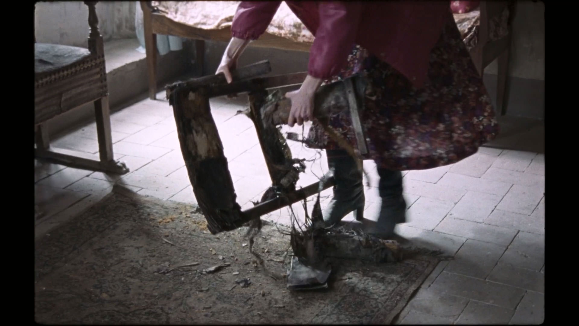 زنی یک صندلی پوسیده را می‌شکند در نمایی از فیلم کیمرا به کارگردانی آلیچه رورواکر