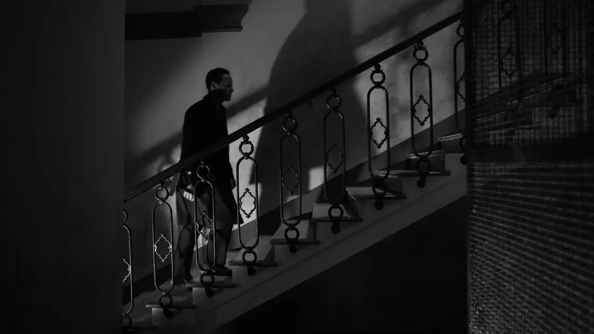 در این تصویر سیاه و سفید از سریال ریپلی استیون زیلیان، اندرو اسکات با سایه بزرگش پشت سرش از پله ها بالا می رود.