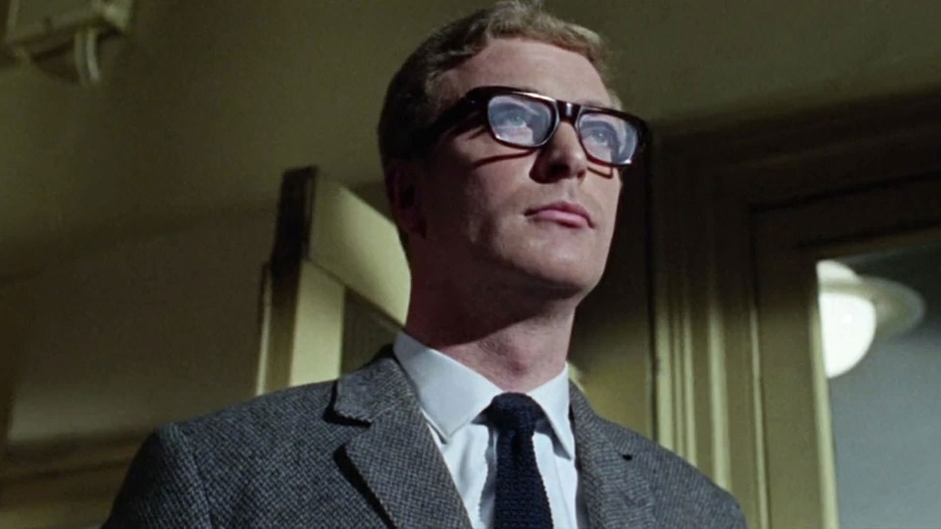 مایکل کین در صحنه‌ای از فیلم «پرونده اپیکور» ساخته سیدنی جی فیوری کت و شلوار و عینک می‌پوشد.