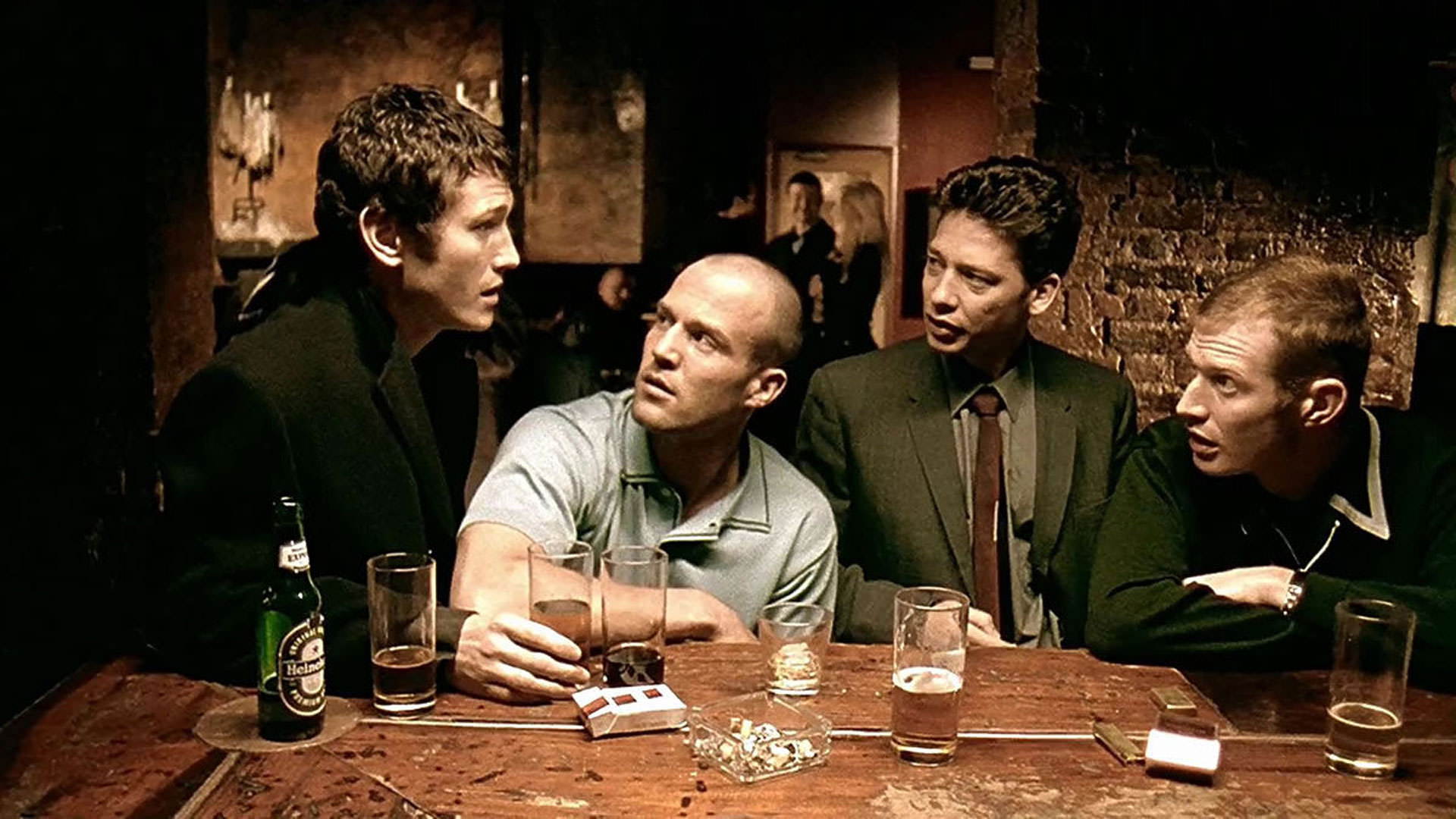 جیسون استاتهام و دکستر فلچر به همراه دو مرد دیگر نشسته داخل یک بار در نمایی از فیلم قفل انبار و دو بشکه باروت به کارگردانی گای ریچی