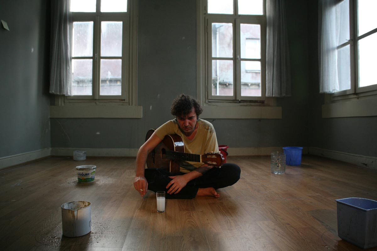 خلیل سزایی نشسته روی زمین درحال نواختن گیتار و کشیدن سیگار در فیلم مربای انجیر