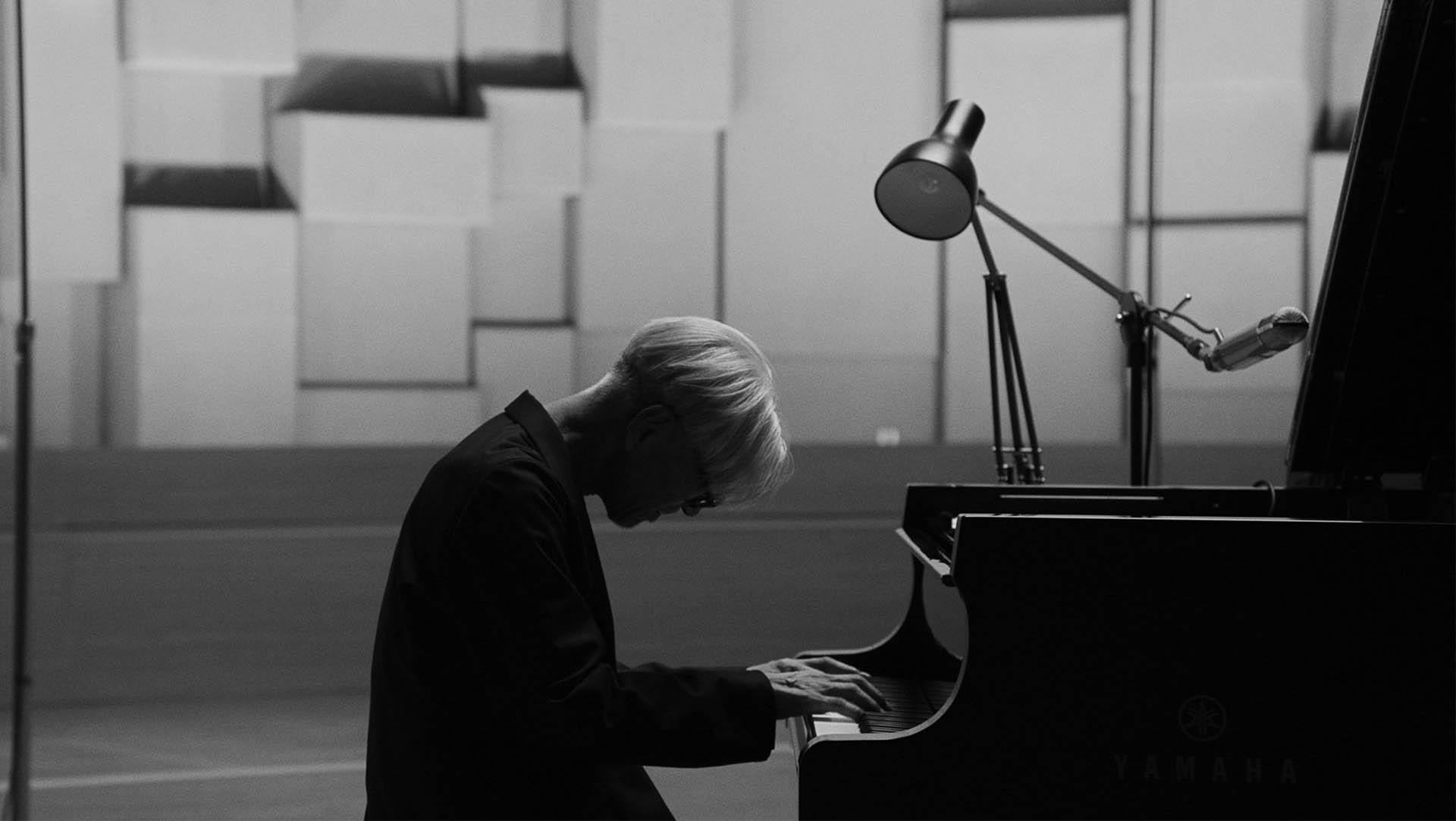 ریوئیچی ساکاموتو خم‌شده روی پیانو در مستند Ryuichi Sakamoto: Opus